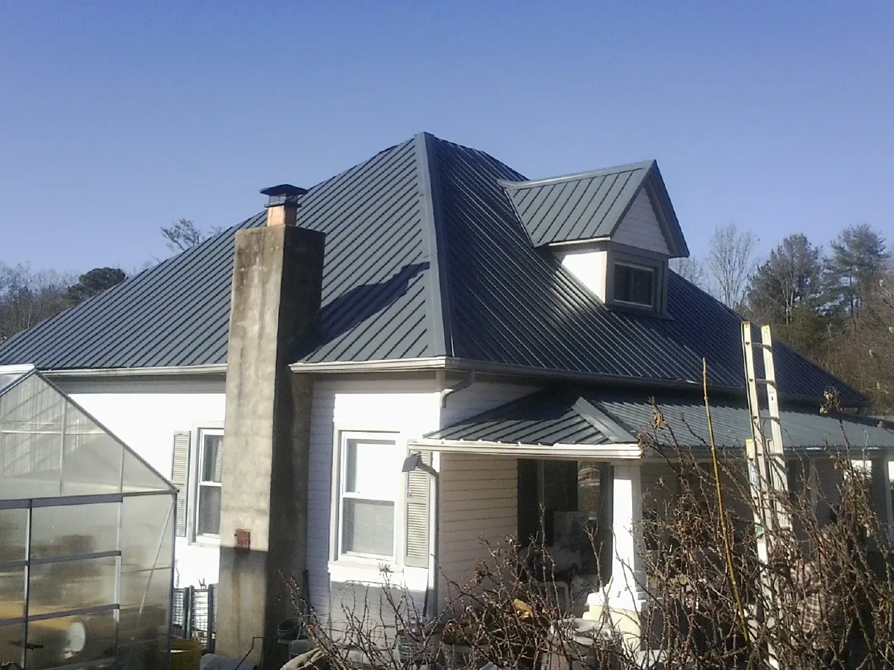 Dark blue standing seam metal roof on a white farmhouse with dormer — Slate & Tile Roof Repair by Roofing Brothers in Saint Peters