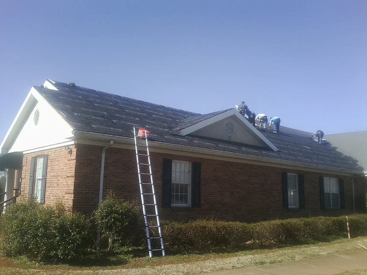 Crew tearing shingles off a brick ranch roof with a ladder set — Emergency Roof Repair work by our crew in Saint Peters