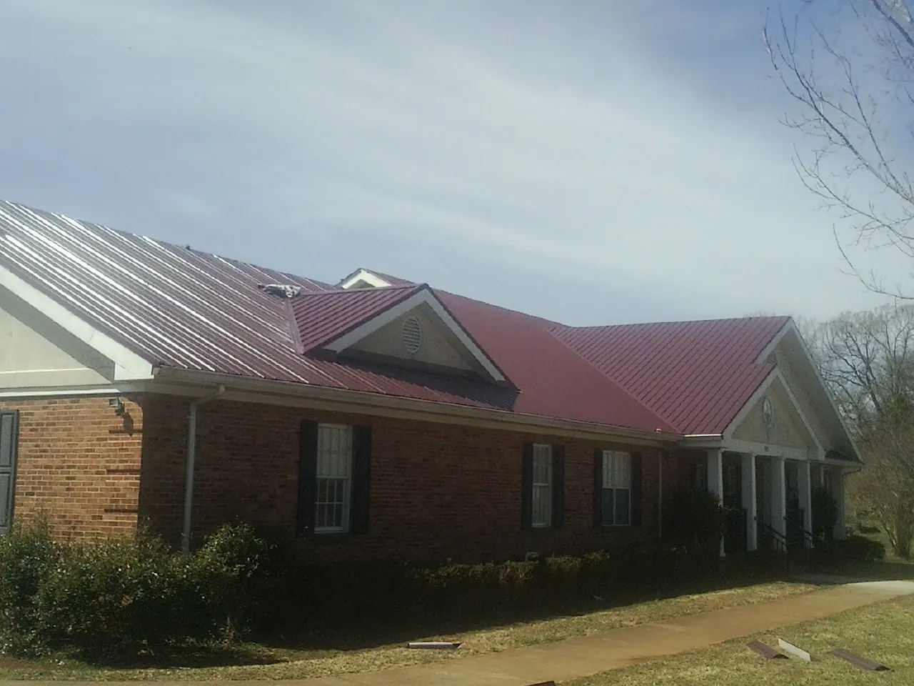 Red metal roof with gabled entries on a long brick building, from a Hail Damage Roof Repair job in Saint Peters