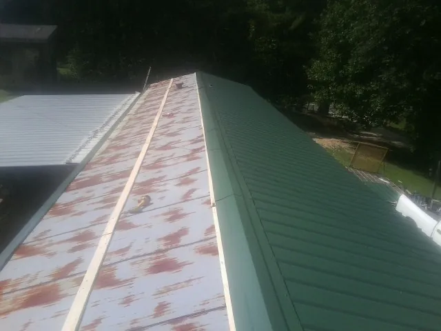 Old rusted panels beside newly installed green metal roofing — Wind Damage Roof Repair by Roofing Brothers in Saint Peters