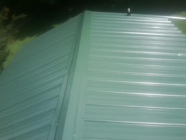 New green metal panels meeting at the ridge of a roof — Flat Roof Repair work by our crew in Saint Peters