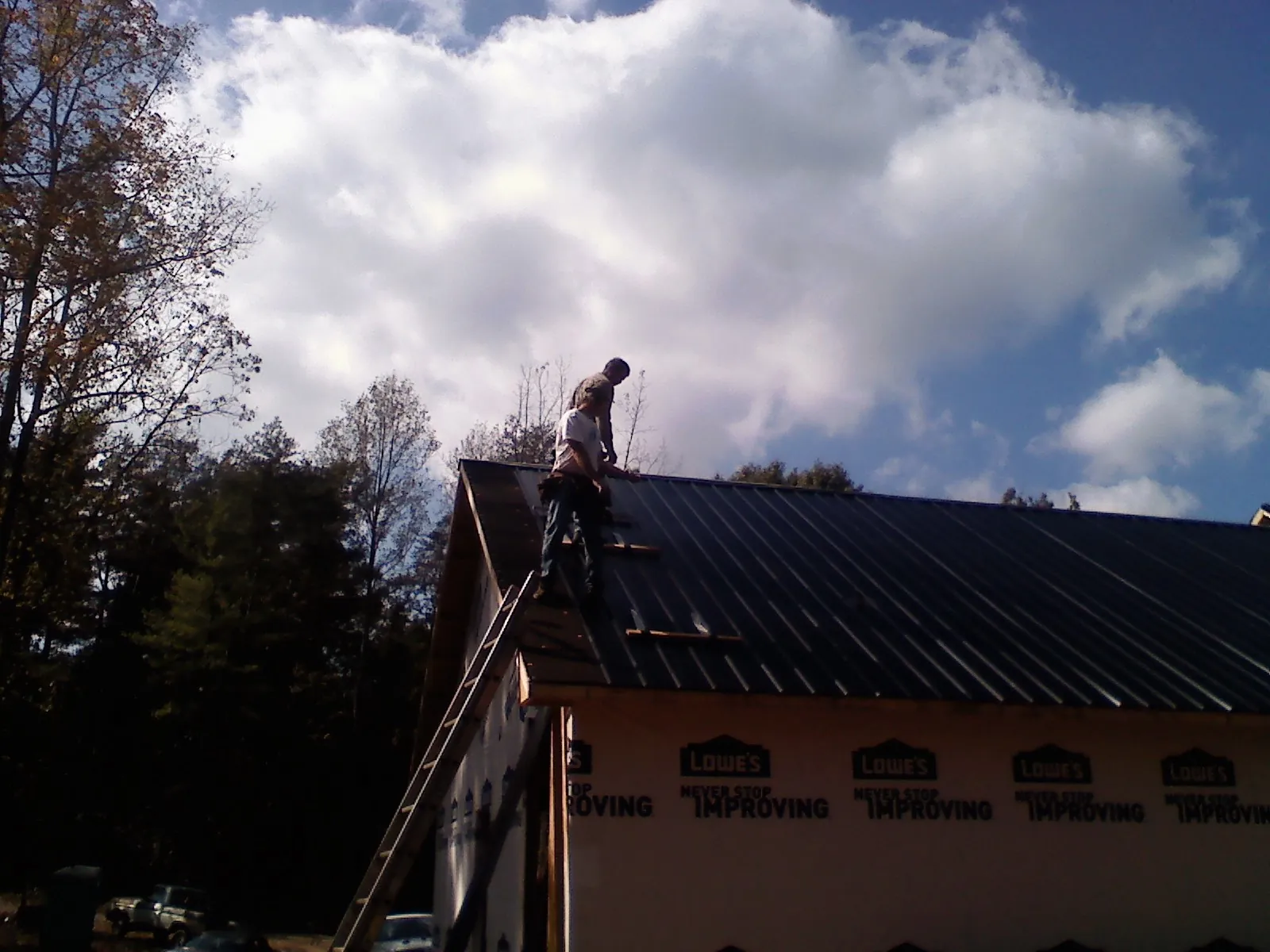 Roofer fastening dark metal panels high against a cloudy sky, from a Roof Inspection job in Saint Peters