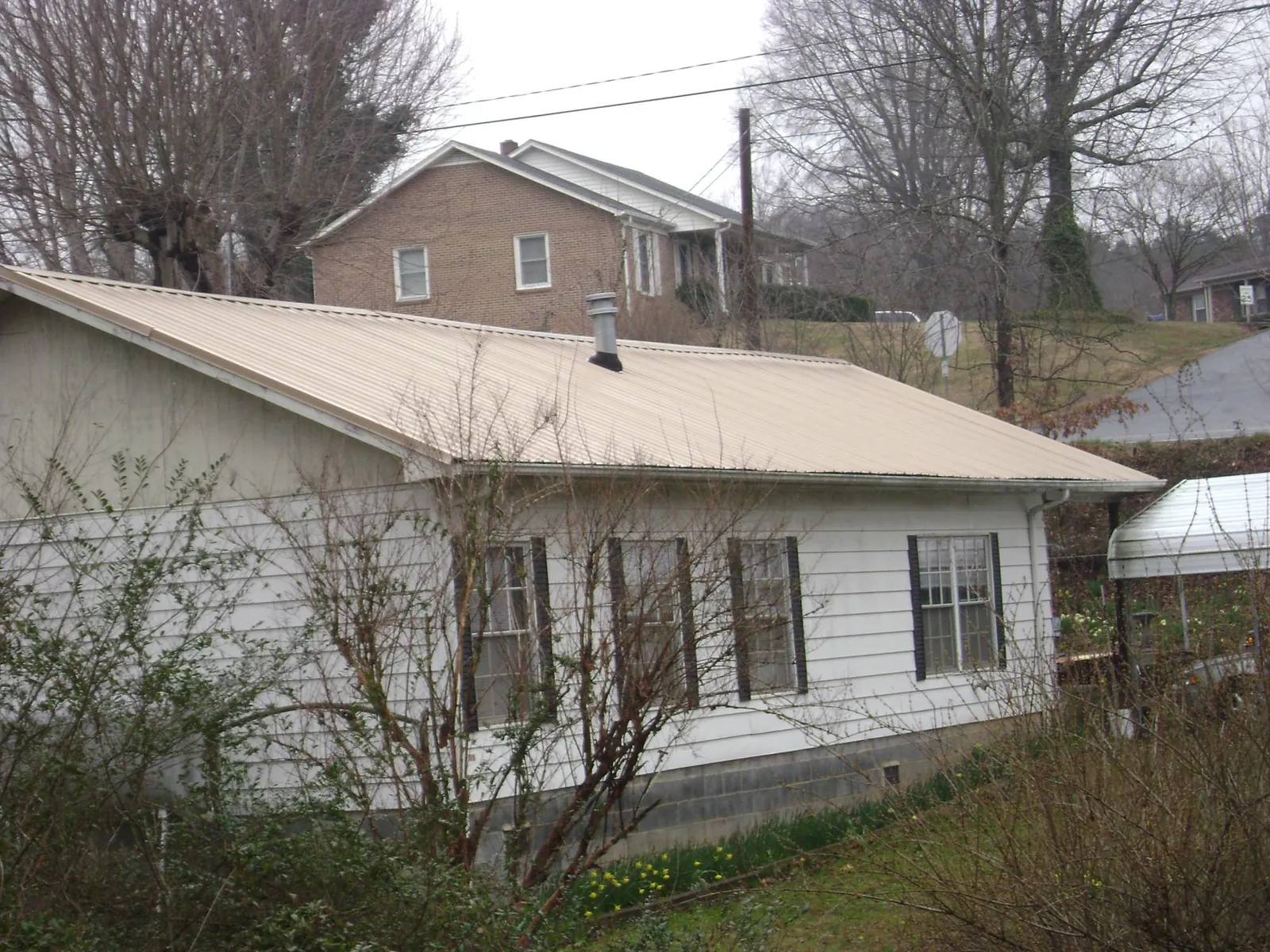 Tan metal roof on a white sided house set into a hillside in Saint Peters