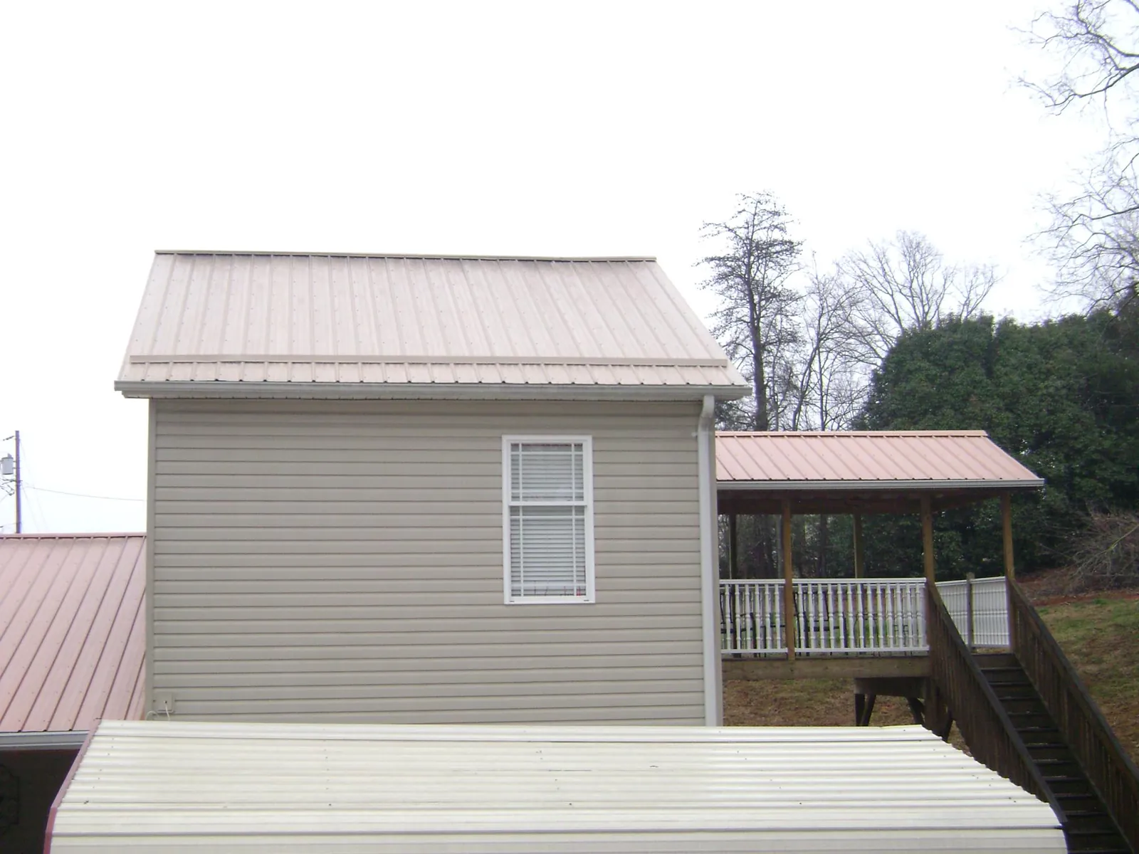 Tan metal roofs on a two story addition and attached porch, from a Roof Replacement job in Saint Peters